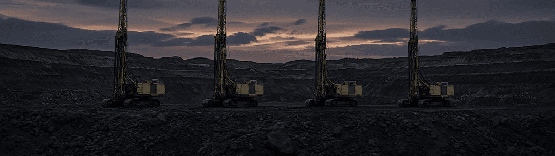 Two surface drill rigs working a dark rock bench in an open-pit mine